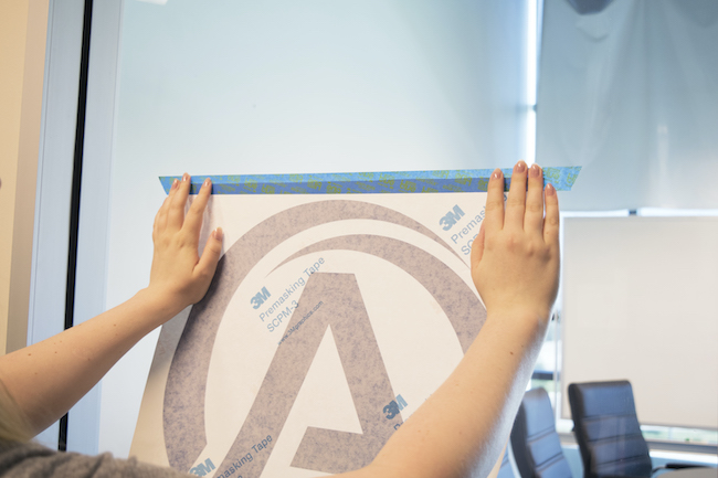 Person using painters tape to create a hinge for the vinyl lettering to be applied