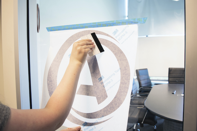 Person using squeegee on vinyl lettering to apply to surface